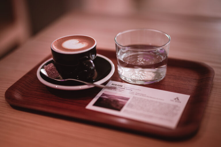 Cup of coffee with latte art, a glass of water and a tasting card served on a wooden tray