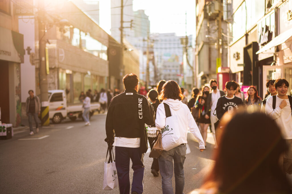 Crowds walking through a Seoul shopping district in warm late-afternoon sunlight