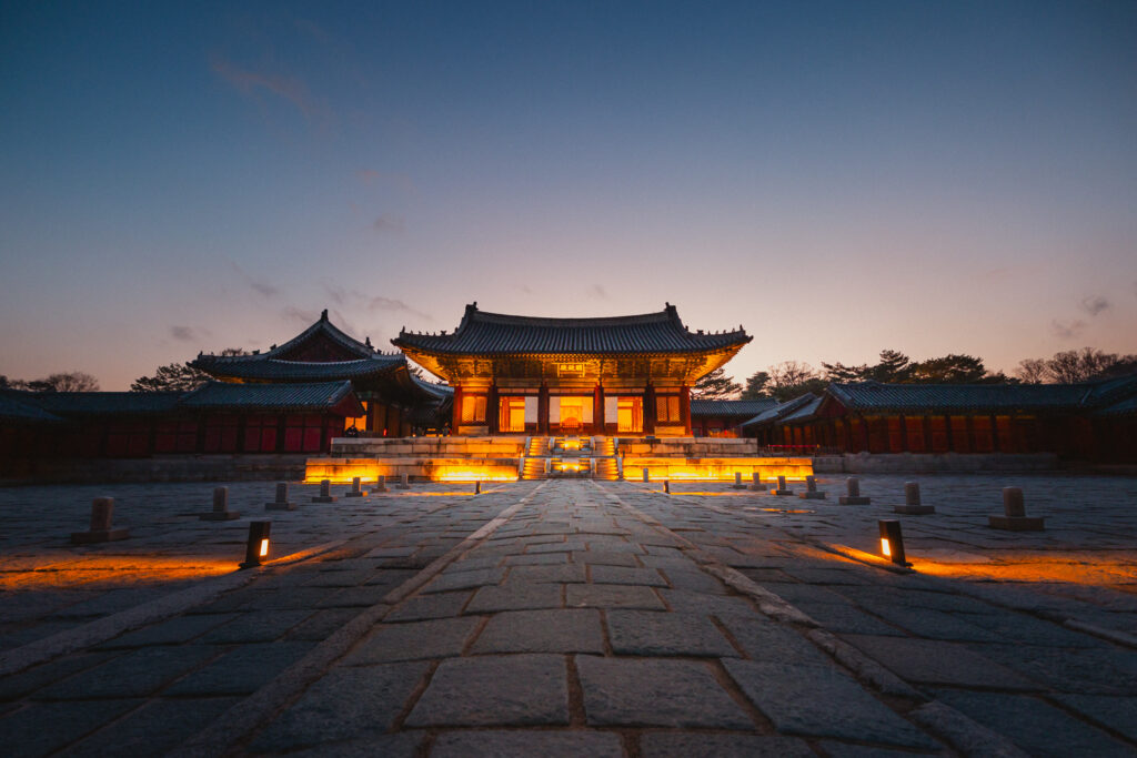 Traditional Korean palace hall illuminated at dusk beneath a fading blue sky in Seoul