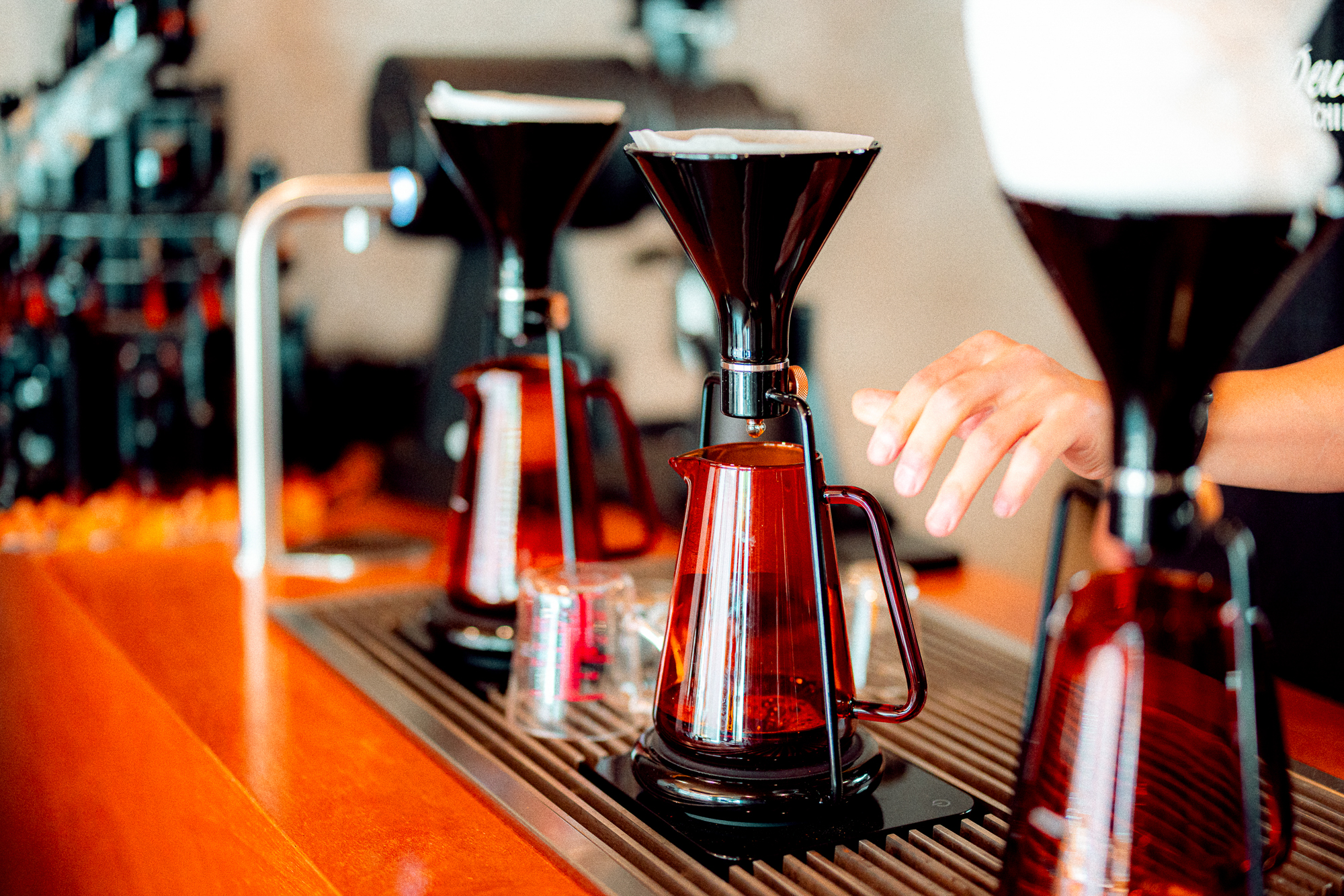Barista preparing pour-over coffee with glass drippers and carafes at a cafe counter