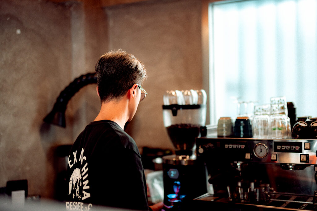 Barista standing beside an espresso machine inside a softly lit modern cafe