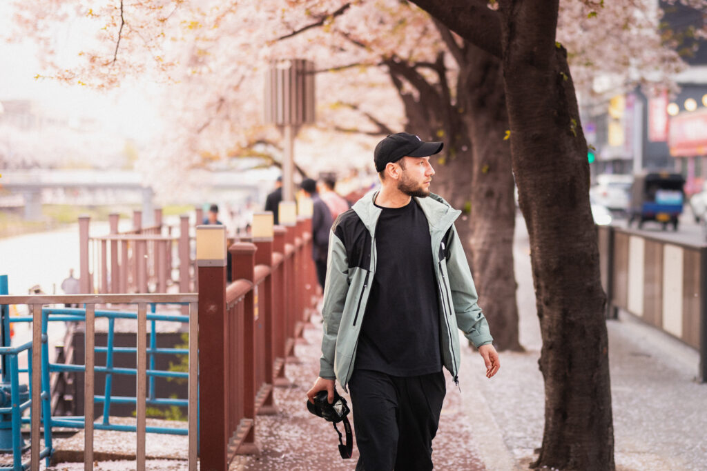 Man carrying a camera while walking beneath cherry blossoms on a spring street in Seoul