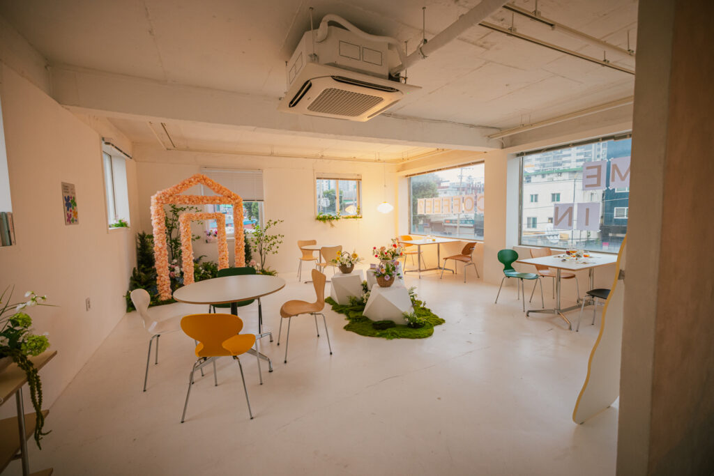 Bright minimalist cafe interior with colorful chairs, floral decorations and large windows overlooking a Seoul street