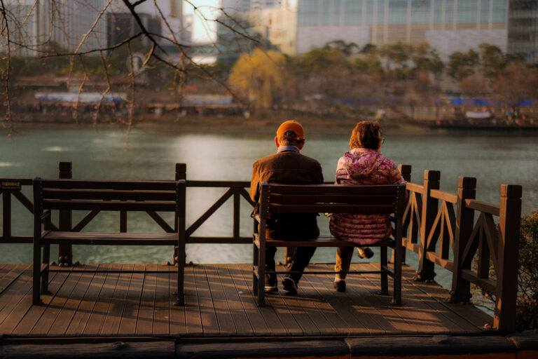 Older couple sitting together on a lakeside bench in Seoul during golden hour