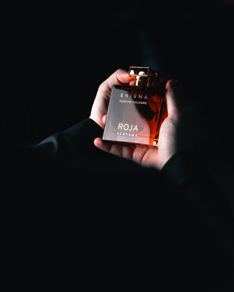 Hands holding a bottle of Roja Parfums Enigma Parfum Cologne against a dark background