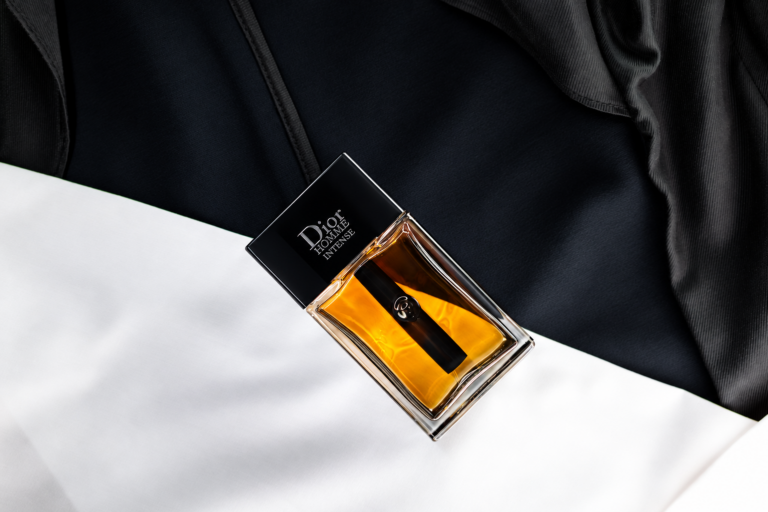 Bottle of Dior Homme Intense perfume resting on black and white fabric in dramatic light