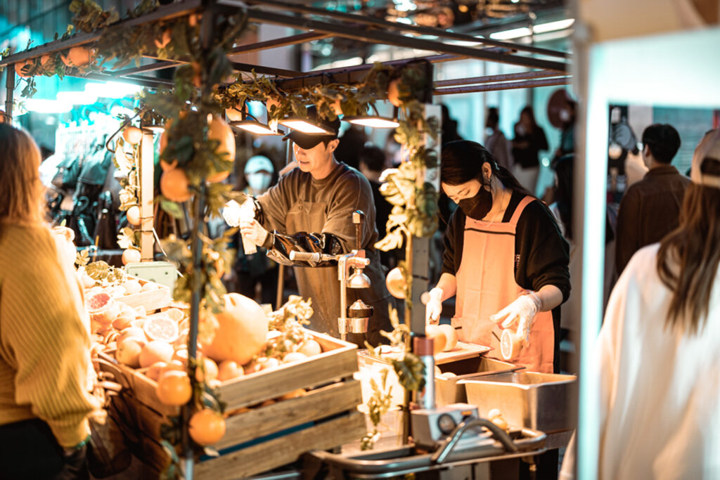 Vendors preparing fresh fruit drinks at a busy indoor market stall in Seoul
