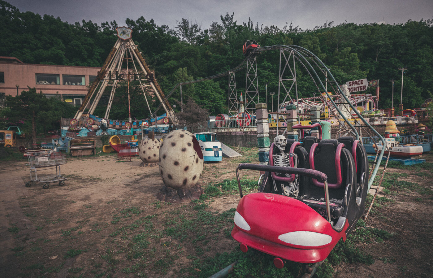 Skeleton prop seated in a red roller coaster car, with an empty Viking ship ride and other rides behind it.