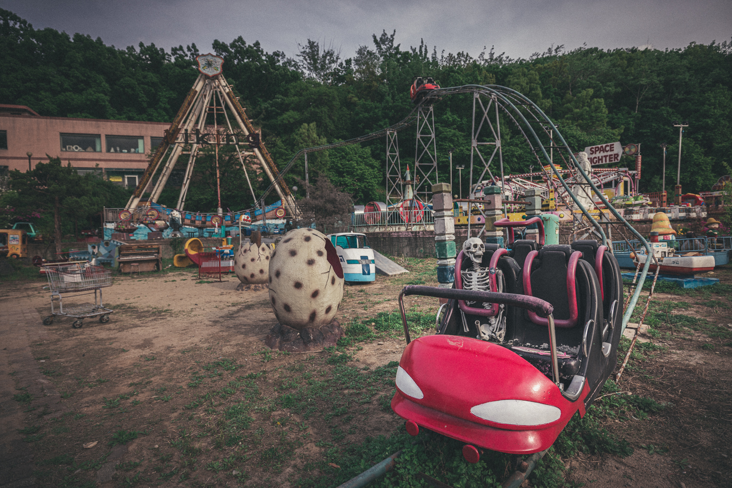 Skeleton prop seated in a red roller coaster car, with an empty Viking ship ride and other rides behind it.
