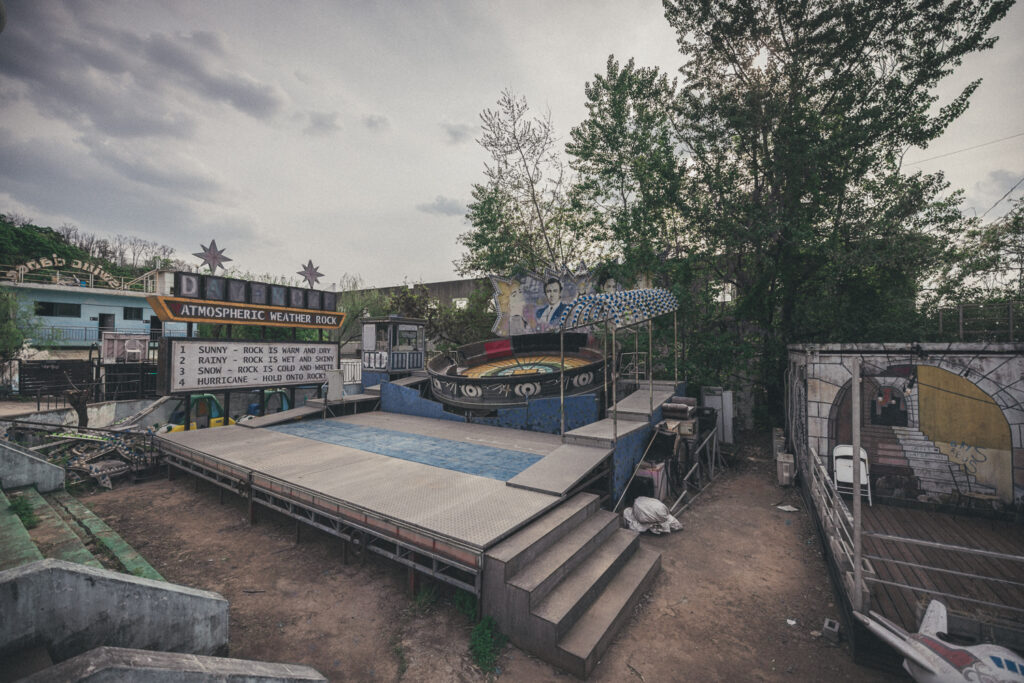 Empty ride platform with steps, a weather sign and a circular ride at Yongma Land.