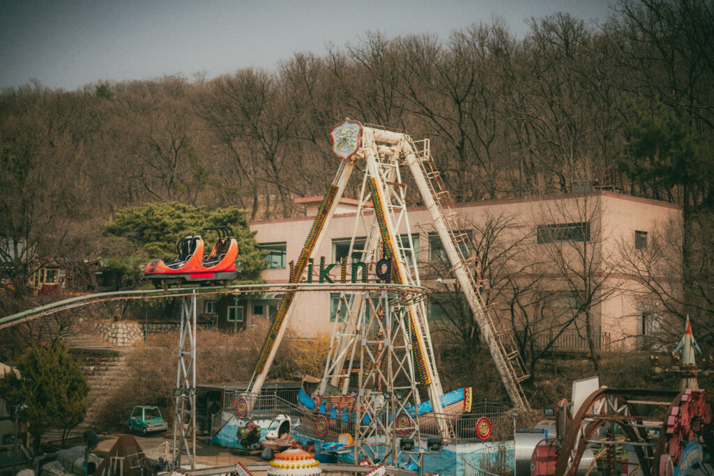 Viking ship ride and a red car on an elevated track amid smaller rides, with a bare wooded hillside behind.